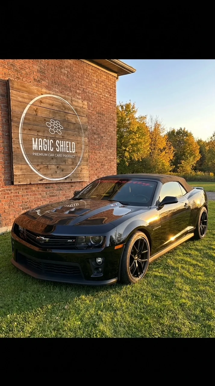 A customer’s glossy black Camaro beside the Magic Shield wall