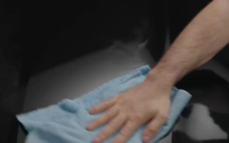 A soft blue microfibre towel wiping a finished black vehicle panel