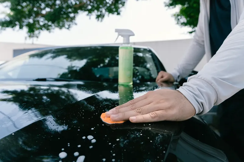 A person gliding a clay bar over lubricated vehicle paint.