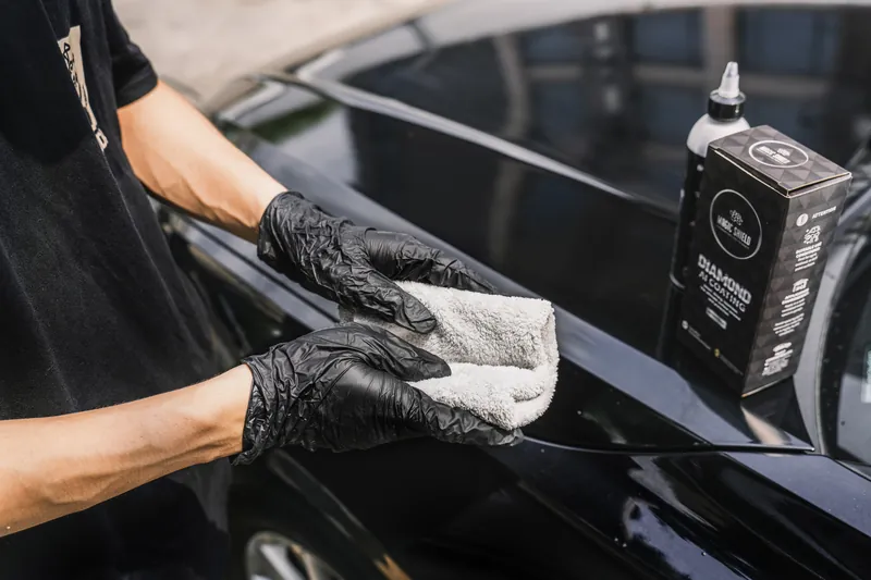 A Diamond AI bottle and box beside a person wiping black vehicle paint.