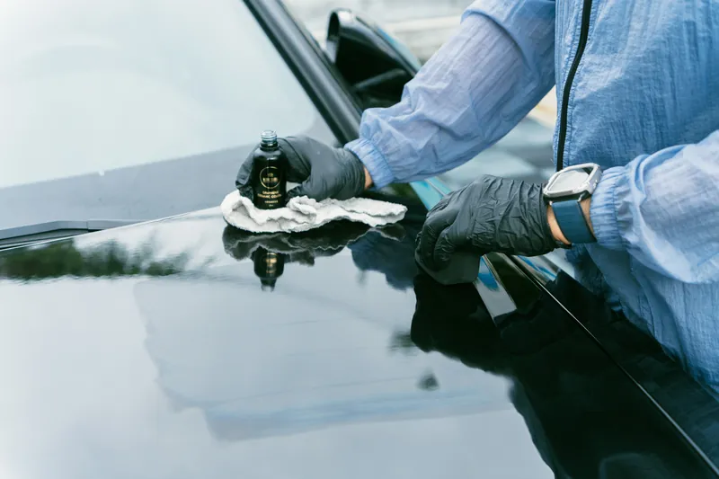 A person wiping a dark vehicle beside a Magic Shield Graphene Coating bottle.