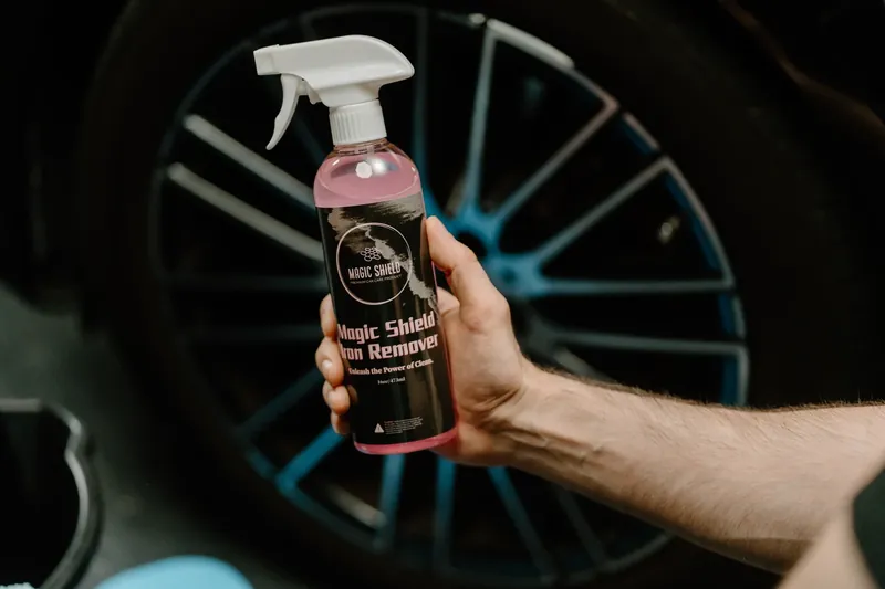 A Magic Shield Iron Remover bottle held beside a vehicle wheel.