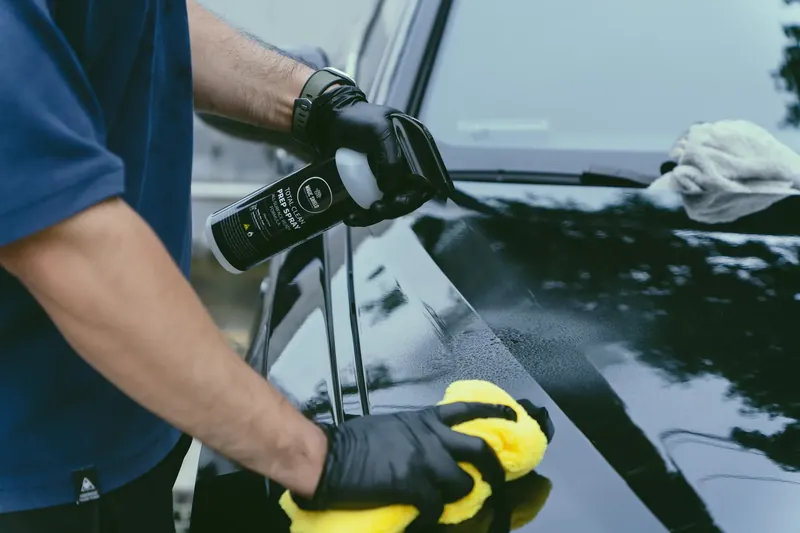 A person wiping vehicle paint with a towel while holding Magic Shield Prep Spray.